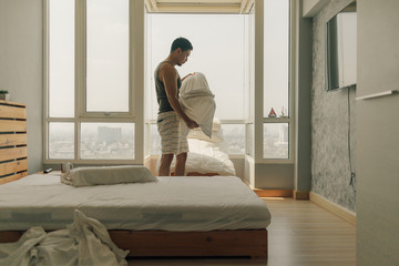 Asian man is cleaning his bedroom with warm summer light.