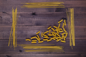Dry pasta- spaghetti and fusilli. Types and shapes of uncooked italian macaroni on wooden background. Space for text.