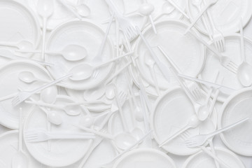 White disposable plastic tableware. Plastic plates, forks, spoons, knives. Abstract background of...