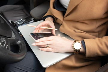 Young woman holding a phone. Workplace in car with laptop. Close up 