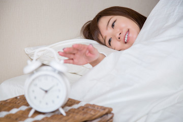 目覚まし時計で起きる女性（女性にピント）