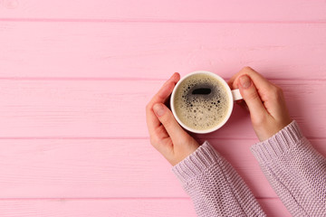  Cup of coffee with frothy in female hands on wooden table. Top view.