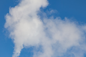 Obraz premium White harmful smoke coming out of the red-and-white pipes with mobile communication antennas at a factory in the city center against the background of a clear blue sky. Environmental problems.