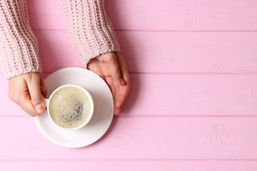  Cup of coffee with frothy in female hands on wooden table. Top view.