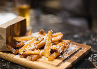 delicious homemade fried potato with shredded cheese on wooden plate, blurred beer glass as background