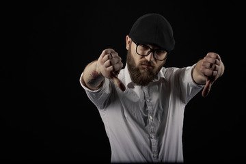 young handsome man in glasses with a beard and a mustache in a black cap and a white shirt shows a...
