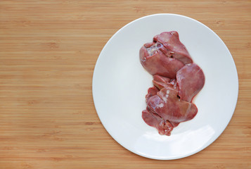 Raw fresh chicken liver in white plate on wooden board background.
