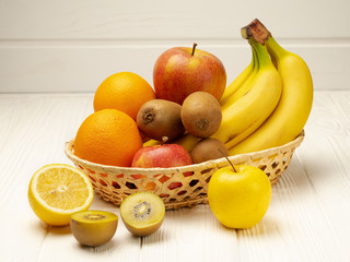 Assorted fruits in a wicker basket on a white wooden background