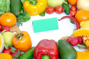 Vegetables and fruits closeup on wooden background. Mango, radish, yellow pepper, red pepper, lemon, cucumber, dill, tangerine, parsley. In the middle of the cutting Board and a sheet of green paper