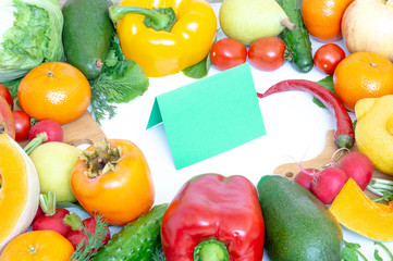 Vegetables and fruits closeup on wooden background. Mango, radish, yellow pepper, red pepper, lemon, cucumber, dill, tangerine, parsley. In the middle of the cutting Board and a sheet of green paper