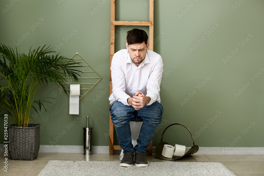 Wall mural Man suffering from diarrhea while sitting on toilet bowl at home