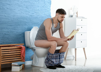 Man reading book while sitting on toilet bowl at home
