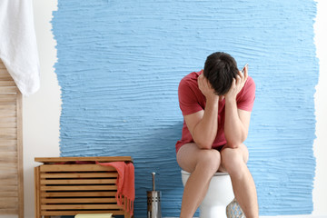 Man suffering from diarrhea while sitting on toilet bowl at home