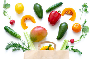 Vegetables and fruits in paper bag on white background. Mango, radish, yellow pepper, red pepper, lemon, cucumber, dill, tangerine, parsley.