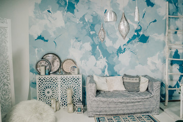 photo studio with white sofa, white bedside table, aluminum decorative plates, designer chandelier against the background of the blue wall