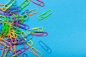 a bunch of multi-colored paper clips scattered on a blue background, office concept