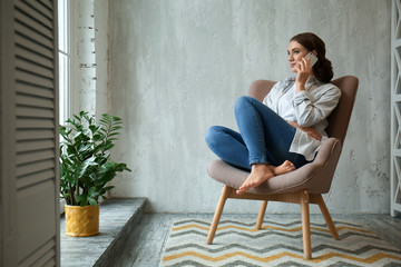 Beautiful young woman talking by mobile phone at home