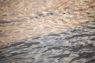 Background water. Asphalt and sand. Stream of water over the asphalt. Beautiful sea background with sand. Fine sand under water. Water texture Waves on the water. Different wavelength. The laws of phy