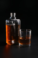 Glass and bottle of whiskey on black background