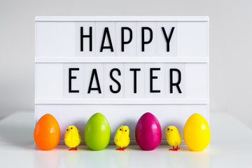 Vintage lightbox with happy Easter greetings, colorful eggs and decorative chicks on the table