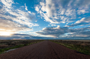 Long straight sealed road disappears into the distant horizon under a sunset sky full of clouds in the outback