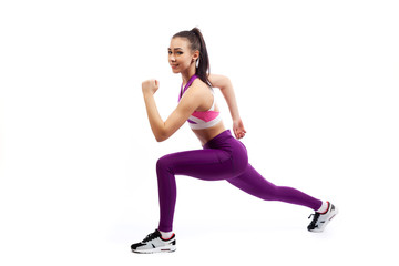Fototapeta na wymiar A young woman coach in a sporty short top and gym leggings makes lunges by the feet forward, hands are held out to the side on a white isolated background in studio