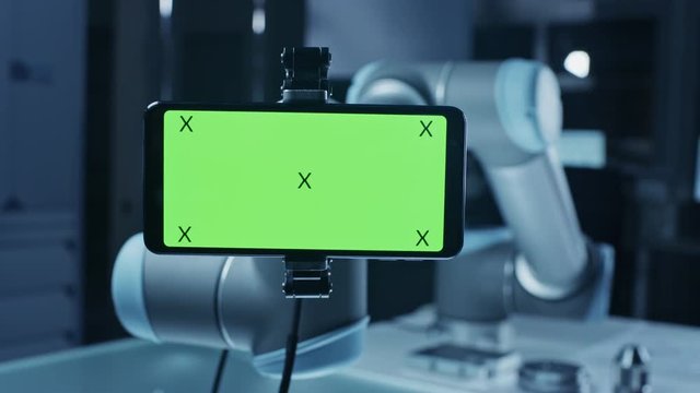 Robot Arm Holding Green Mock-up Screen Smartphone in Landscape Mode, Smoothly Moving into Focus. Industrial Robotic Manipulator End Effector Holds Mobile Phone with Chroma Key Display. 