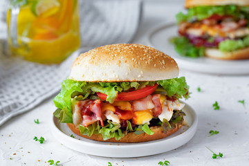 Fresh tasty chicken burger on white table. Two chickenburgers with bacon, lettuce, tomato, sauce, cheese and chili pepper, close-up
