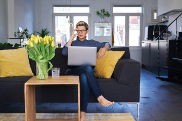 Business woman with short hair and glasses working on laptop at modern apartment, sunny daylight. Concept of young entrepreneur works on start-up.