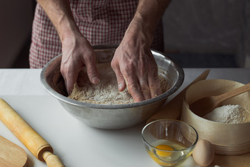 A handful of flour with egg on a rustic kitchen. Against the background of men's hands
