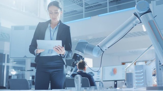Stylish Female Industrial Robotics Engineer Uses Tablet Computer to Program and Manipulate Robot Arm for Lifting, Moving Objects. Technology Research Facility for Machine Learning and Cloud Computing