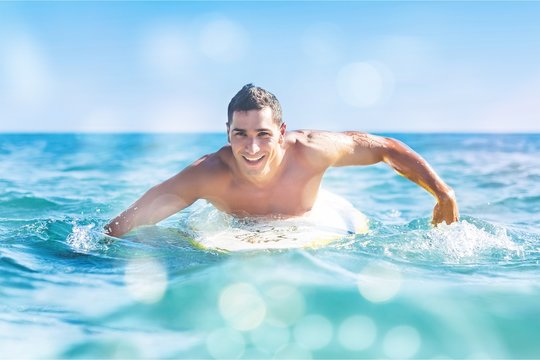 Handsome young surfer floating in blue water