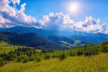 Fototapeta premium Amazing nature, summer daytime landscape. Green mountainside in sunlight and blue sky with clouds and sun beams. Outdoor travel background