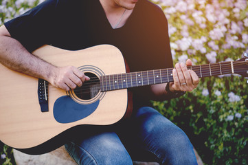 Fototapeta premium Picture of a guitarist, a young man playing a guitar while sitting in a natural garden,music concept