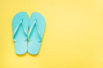 Blue beach flip flop on punchy yellow background. Summer tropical vacations.