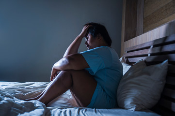 young sad and depressed fat and chubby Asian girl feeling upset and desperate crying on bed at home...