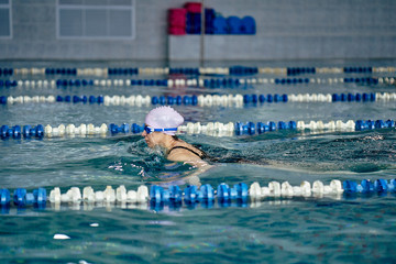 Female athlete in a green-black swimsuit is swimming in the style of breaststroke. Splashes of...