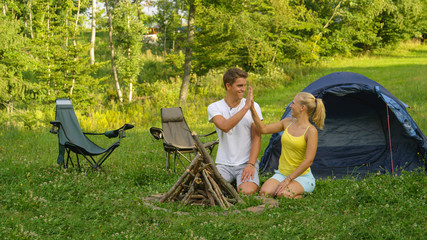 Joyful haired blonde girl high fives her boyfriend after collecting firewood.