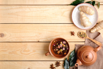 Tea ceremony setting with tea cup, tea pot, spoon of dried tea, anise star, ginger root on play, green leaves on wooden background. Flat lay composition. Top view