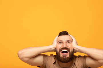 Indoor shot of amazed excited man doesn`t believe his success, keeps hands on head, stares at...