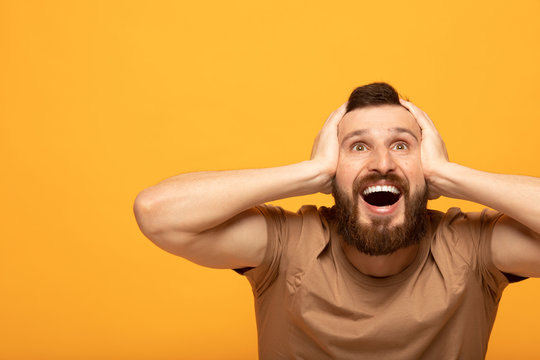 Indoor shot of amazed excited man doesn`t believe his success, keeps hands on head, stares at camera, says omg or wow.