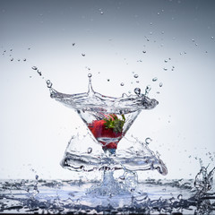 Beautiful frozen nuclear explosion of freshness with splashes of water, in a cocktail glass with strawberries, on a white background.