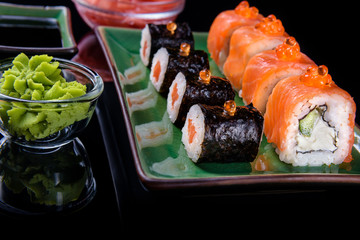Japanese food. A set of various rolls of salmon, eel, shrimp and red caviar, in a beautiful green bowl, on a black background with reflection.