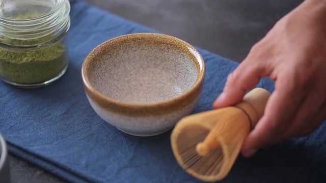 Man preparing green tea matcha in a bowl on blue surface. Drink is a rich source of antioxidants and polyphenols