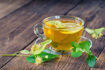 Cup of lime tea, standing on a wooden table, surrounded by fragrant linden flowers, in the rays of sunlight.