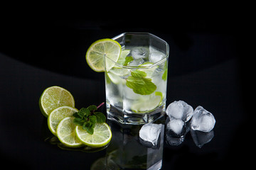 Summer cocktail mojito in glass, sliced lime and ice cubes on black background..