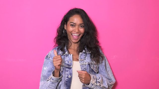footage of pretty asian woman wearing denim jacket smiling and giving thumbs up on pink background