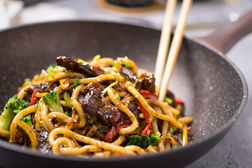 Udon Stir-Fry Noodles with Beef and Vegetables in Wok Pan on Dark Background