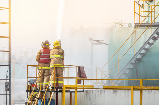 professional firemans brave buddy team assistance in yellow fire fighter uniform holding fire hose nozzle fighting with fire flame in the industrial factory