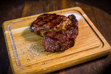 Beef steak on wood board with fork and knife herbs spices and salt